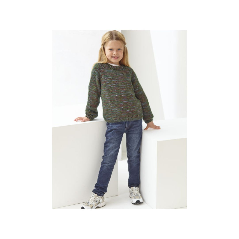A young girl with blonde hair stands on white geometric steps, wearing a green marled knit sweater, blue jeans, and white sneakers.