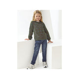 A young girl with blonde hair stands on white geometric steps, wearing a green marled knit sweater, blue jeans, and white sneakers.