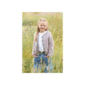 A young girl with blonde hair stands in a field of tall grass, wearing a textured grey and white striped cardigan over a white top and blue jeans.
