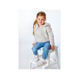 A young girl with blonde hair in a ponytail sits on a white wooden stool against a plain white studio background. She is wearing a chunky, textured knit hooded sweater in a heathered light gray, pink, and blue colorway, paired with blue jeans and white sneakers.