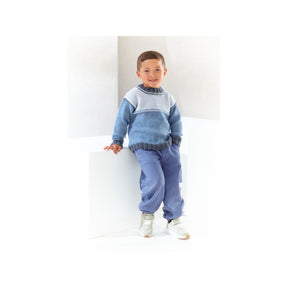 A young boy wearing a blue and grey knit round neck sweater and matching blue sweatpants, standing against a white geometric background.