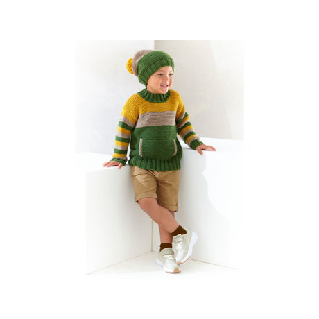 A young child wearing a knitted green and mustard yellow sweater with matching striped knit hat and tan shorts, leaning against a white geometric block in a bright studio setting.