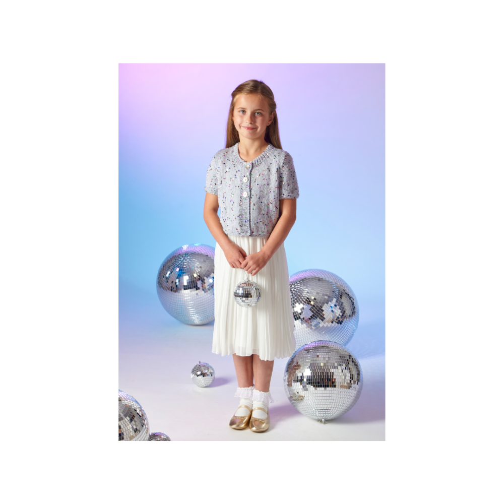 A young girl stands in a studio wearing a short-sleeve patterned top and a pleated skirt, surrounded by several large and small mirrored disco balls against a soft blue-to-purple gradient background.