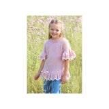 A young girl smiling in a grassy field, wearing a light pink hand-knit short-sleeve top with ruffled sleeves and hem, paired with blue jeans.