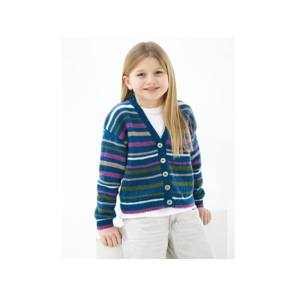 A young girl with long blonde hair wearing a colourful striped knit cardigan over a white t-shirt and light gray pants, standing against a plain white background.