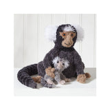 A plush stuffed monkey toy with a dark charcoal body, white fluffy ears and tail tip, tan face and hands, sitting on a white surface against a white paneled background.