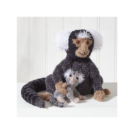 A plush stuffed monkey toy with a dark charcoal body, white fluffy ears and tail tip, tan face and hands, sitting on a white surface against a white paneled background.