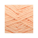 A close-up of peach-coloured chenille yarn strands arranged in a textured crisscross pattern on a white background.