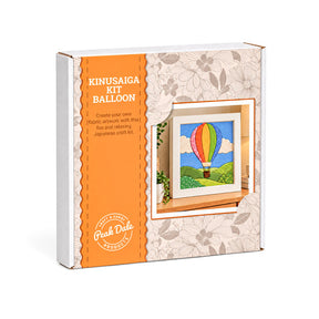 A boxed craft kit labeled 'KINUSAIGA KIT BALLOON' by Peak Dale Products, shown at a slight angle on a white background. The package is white with a large orange panel and floral-patterned paper wrapping around the right side, featuring an illustration of a colorful hot air balloon.