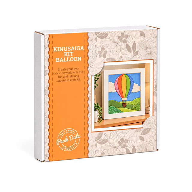 A boxed craft kit labeled 'KINUSAIGA KIT BALLOON' by Peak Dale Products, shown at a slight angle on a white background. The package is white with a large orange panel and floral-patterned paper wrapping around the right side, featuring an illustration of a colorful hot air balloon.
