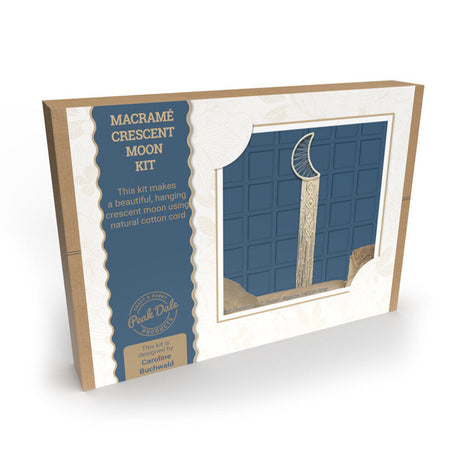 A boxed macramé crescent moon kit shown at an angle on a white background. The package is kraft paper with a large blue label reading 'MACRAMÉ CRESCENT MOON KIT' and a window displaying a completed hanging macramé crescent moon ornament.