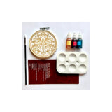 Batik kit with a wooden hoop containing a floral design, a paintbrush, three small bottles of dye  in orange, red, and blue, a white palette, and an instruction booklet on a white background.