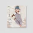 Rico Baby handknitting booklet cover featuring a baby lying on a soft cream blanket, wearing a knitted blue hat and a multicolored knitted romper, with a small knitted sheep toy beside them. The left side includes the title 'The little Rico Baby handknitting booklet' and the RICO BABY logo.
