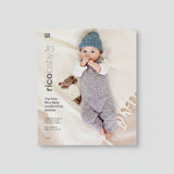 Rico Baby handknitting booklet cover featuring a baby lying on a soft cream blanket, wearing a knitted blue hat and a multicolored knitted romper, with a small knitted sheep toy beside them. The left side includes the title 'The little Rico Baby handknitting booklet' and the RICO BABY logo.