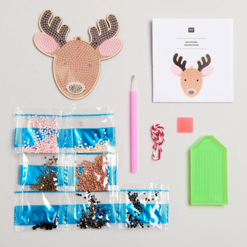 A flat-lay of a Christmas reindeer mosaic craft kit on a light gray background, including a finished reindeer head, instruction card, pink candle, bead packets, candy canes, a pink square, and a green backing sheet.