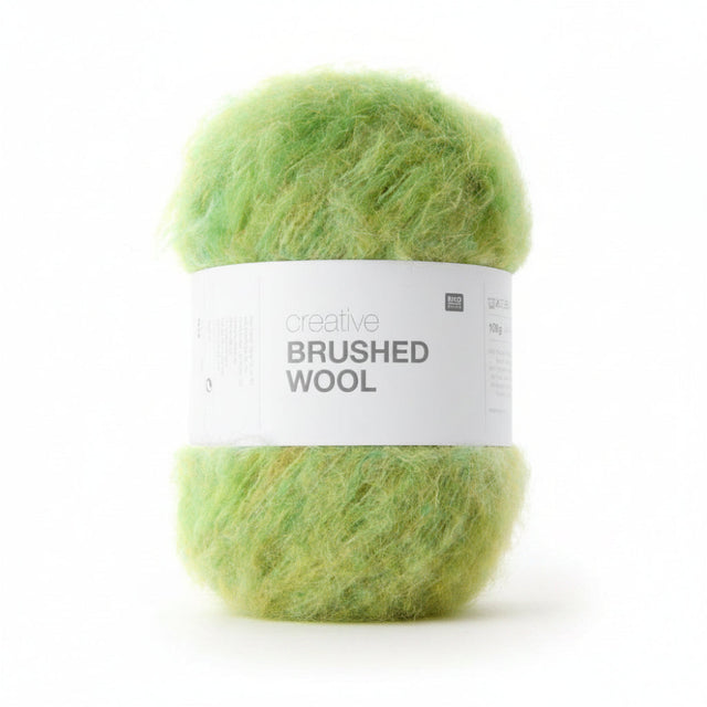 A ball of fluffy lime green yarn wrapped in a white paper band labeled 'creative BRUSHED WOOL' on a plain white background.