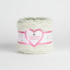A roll of Chenillové Dégradé yarn in a soft mint green color, wrapped with a pink and white paper label featuring a glittery heart.