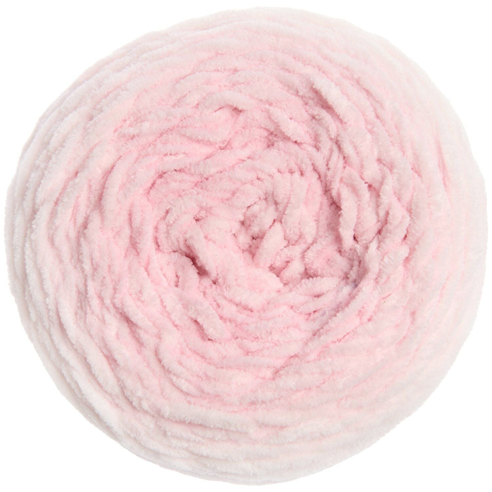 A top-down view of a fluffy, chunky circular skein of yarn in a soft light pink color, isolated on a white background.