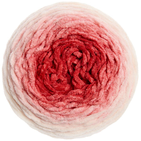 A top-down view of a round ball of plush, fuzzy yarn with a color gradient transitioning from off-white at the outer edges to light pink and deep red in the center, isolated on a white background.