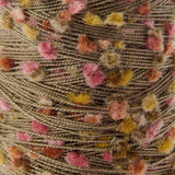 Close-up of a textured yarn ball with a chunky, fuzzy pom-pom effect in a warm taupe-brown base with scattered pink, mustard yellow, and rust-orange flecks.