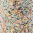 Close-up of a wound spool of variegated yarn with a sage green base and fuzzy pom-pom accents in pink, peach, yellow, and gray.
