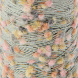 Close-up of a wound spool of variegated yarn with a sage green base and fuzzy pom-pom accents in pink, peach, yellow, and gray.