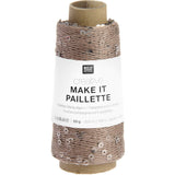 A spool of Rico Design Creative Make It Paillelette yarn, featuring a white paper label with black text and a brown cardboard core, set against a plain white background.