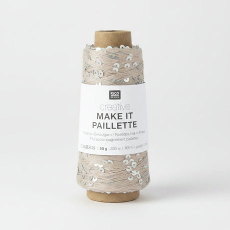 A spool of Rico Design Creative Make It Pailleçte yarn thread, featuring a white paper label with black text and silver sequins on a light beige thread wound around a brown cardboard core, set against a plain white background.