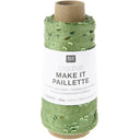 A spool of green decorative twine with a white paper label that reads 'RICO DESIGN creative MAKE IT PAILLETTRE'. The twine has a textured, slightly shiny finish with small green leaf-like accents.