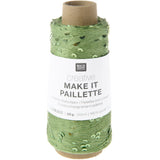 A spool of green decorative twine with a white paper label that reads 'RICO DESIGN creative MAKE IT PAILLETTRE'. The twine has a textured, slightly shiny finish with small green leaf-like accents.