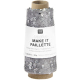 A spool of silver thread with attached sequins, wrapped in a white paper label that reads 'RICO DESIGN creative MAKE IT PAILLETTE'.