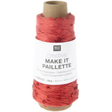 A spool of Rico Design creative 'Make It Paillette' yarn in a coral pink shade, wound on a brown cardboard core with a white paper label.
