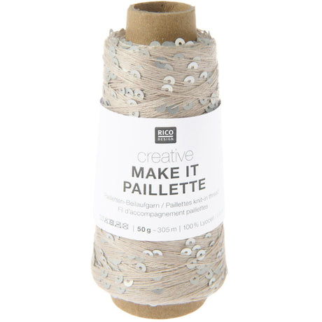 A spool of Rico Design Creative Make It Pailleçte yarn thread, featuring a white paper label with black text and silver sequins on a light beige thread wound around a brown cardboard core, set against a plain white background.