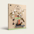 A styled product photo for a crochet and decor kit titled 'The lovely world of RICORUMI' featuring Halloween-themed crocheted ghost figures, a black spider, orange pumpkin decorations, a black candle, and a small table setup against a beige background with decorative branches.