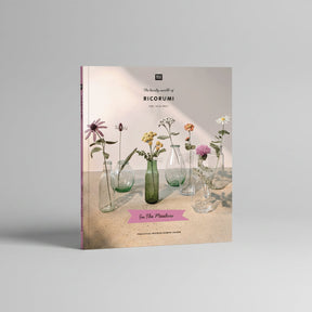 A book cover titled "The lovely world of RICORUMI" featuring several glass vases with dried and fresh flowers on a tabletop against a soft beige background. The cover includes the publisher mark "BLOOM" at the top and a pink banner reading "In The Meadow" near the bottom.