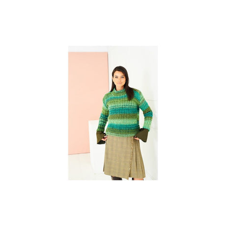 A woman modeling a green and blue striped knit sweater with olive green cuffs, paired with a beige plaid skirt, standing against a minimalist studio background with a pink panel.
