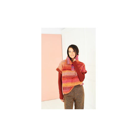A woman modeling a colourful striped knit sweater vest over a rust red long-sleeve top and brown tweed trousers, standing against a minimalist white and pink background.