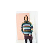 A woman wearing a chunky, multicoloured striped knit turtleneck sweater, standing in front of a minimalist pink and white wall.