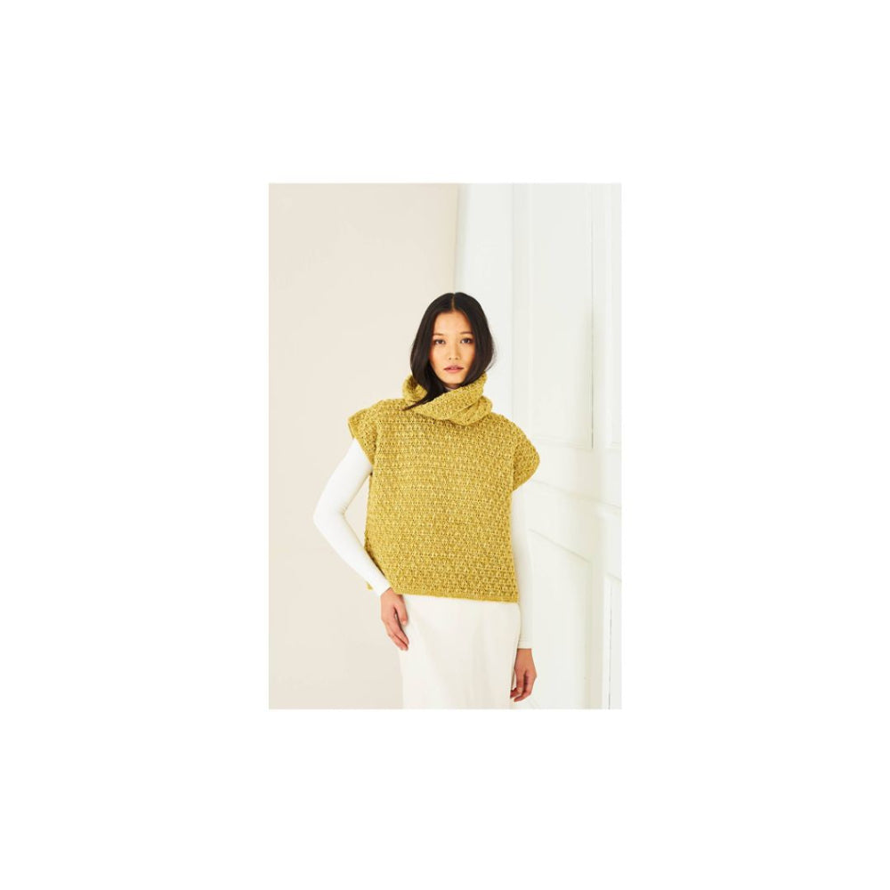 A woman wearing a textured mustard yellow crochet mock-neck sweater vest over a white long-sleeve top and white pants, standing against a minimalist off-white background.