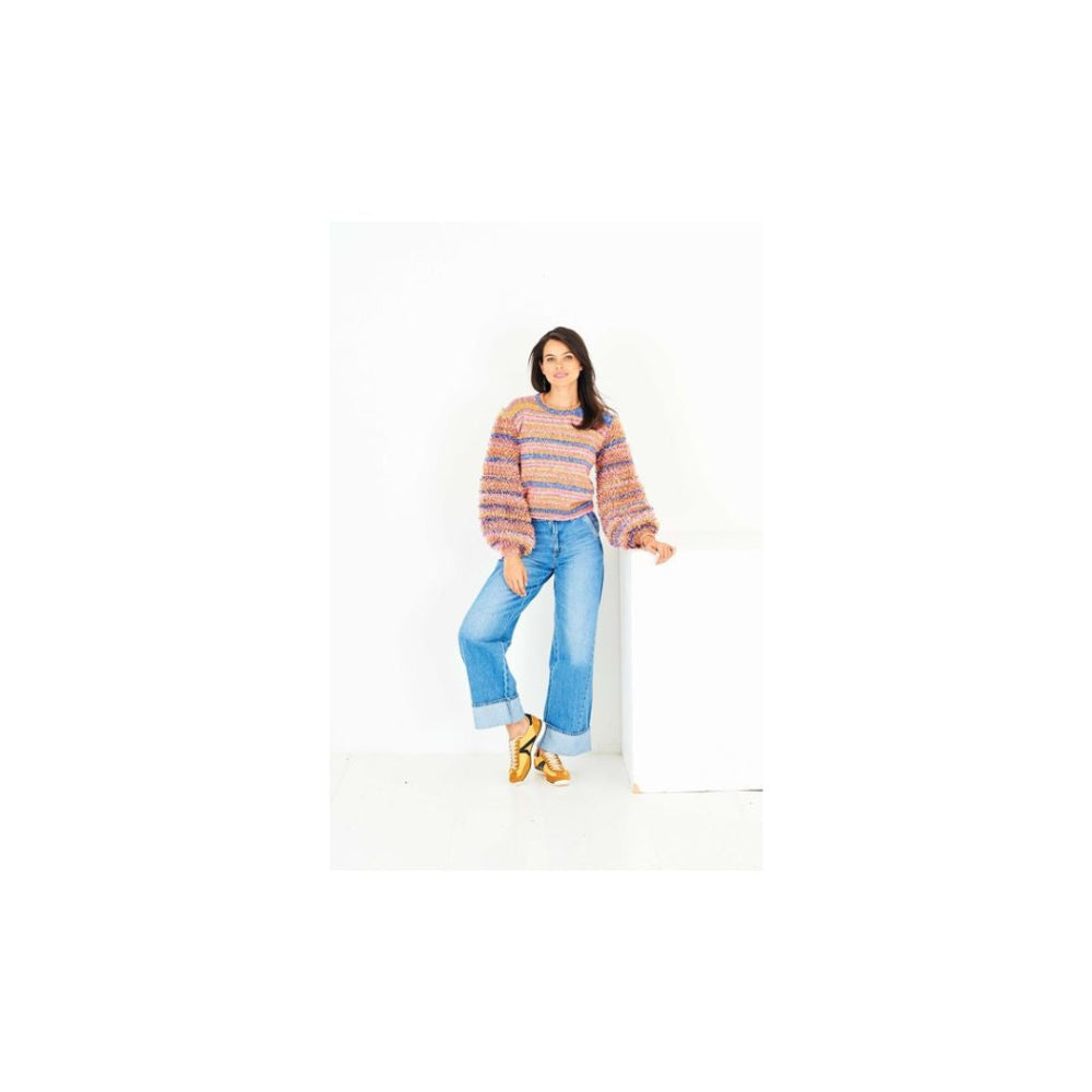 A woman modeling a multicolour striped knit sweater and light blue wide-leg jeans, standing against a white studio background.