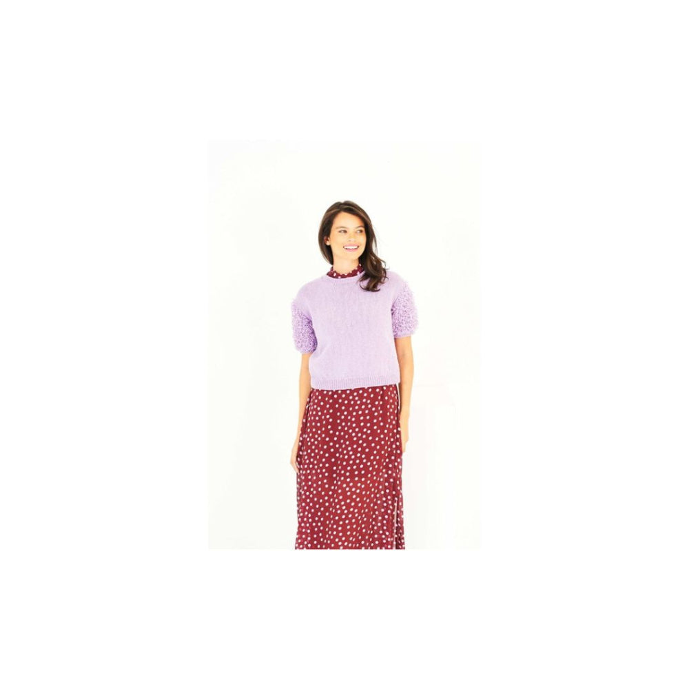 A woman modeling a short-sleeve lavender knit top with textured puff sleeves and a red skirt with a white polka dot pattern, set against a plain white background.