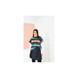 A model wearing a colourful, striped knit tank top with blue, green, orange, and purple tones, layered over a white long-sleeve top and a dark pleated skirt, standing against a minimalist white and pink wall.