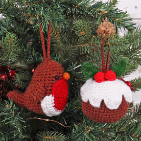 Two handmade crocheted Christmas ornaments hanging on a green Christmas tree. One ornament is a brown bird with a red beak and white chest.