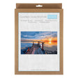 A counted cross stitch kit in a brown kraft paper sleeve with a white front label showing a sunset dock over water and the text 'Counted Cross Stitch Kit' and 'Trolli'.