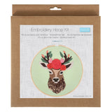 An embroidery hoop kit in its original brown kraft paper packaging, featuring a printed illustration of a deer with a floral crown on a light green background.