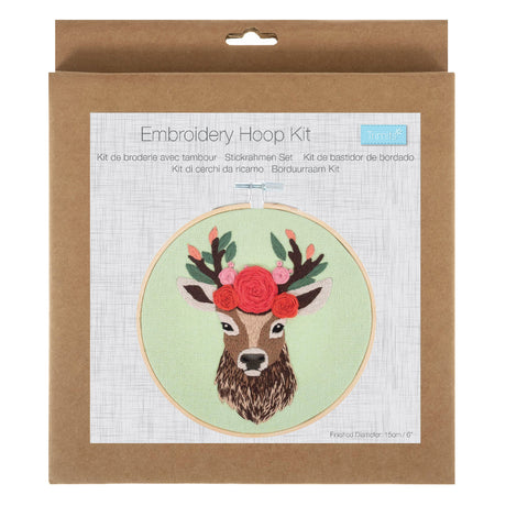 An embroidery hoop kit in its original brown kraft paper packaging, featuring a printed illustration of a deer with a floral crown on a light green background.