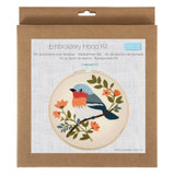 A packaged embroidery hoop kit in a brown kraft paper box, showing a printed sample of a bird embroidery design with blue, orange, green, and black details on a white background.