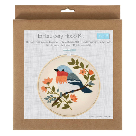 A packaged embroidery hoop kit in a brown kraft paper box, showing a printed sample of a bird embroidery design with blue, orange, green, and black details on a white background.