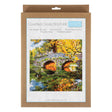 A counted cross stitch kit in its original brown kraft paper packaging, featuring a colorful illustration of a stone bridge over a reflective pond surrounded by autumn trees.
