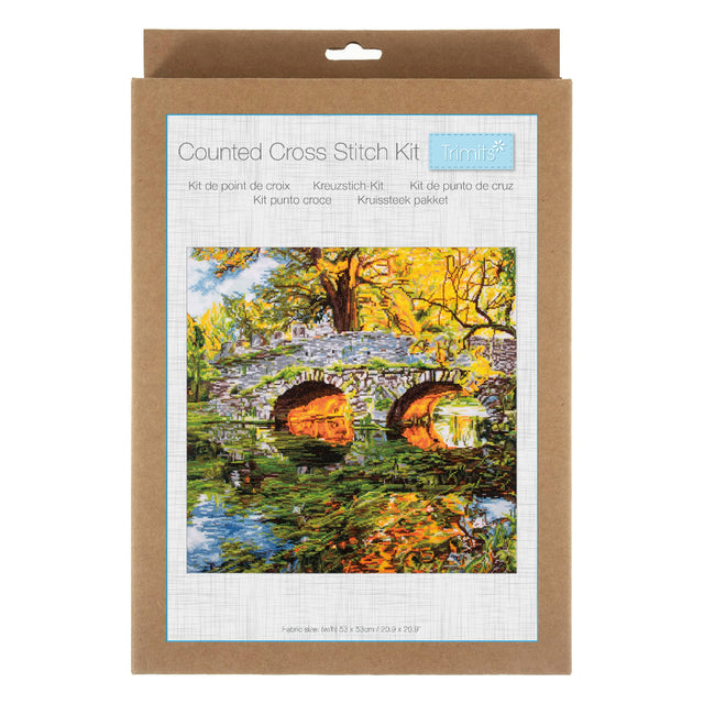 A counted cross stitch kit in its original brown kraft paper packaging, featuring a colorful illustration of a stone bridge over a reflective pond surrounded by autumn trees.